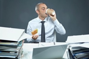 Businessman eating sandwich with coffee at his workplace